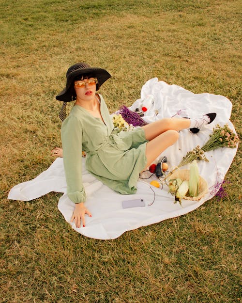 Woman Sitting on a Blanket in Dress, Hat and Sunglasses