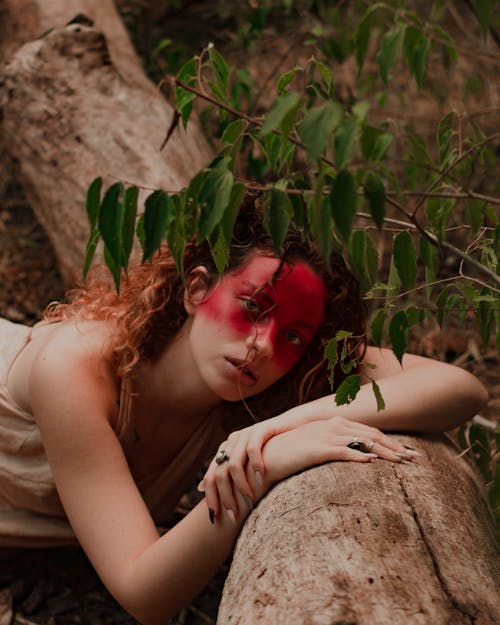 Woman with Half Painted Face Lying on Tree Trunk