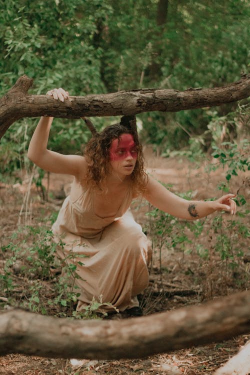 Woman in Face Paint Crouching Under Branch