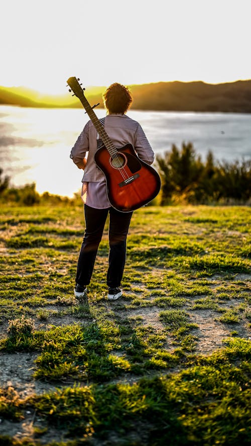 Free Man with a Guitar Standing on Lakeside Stock Photo