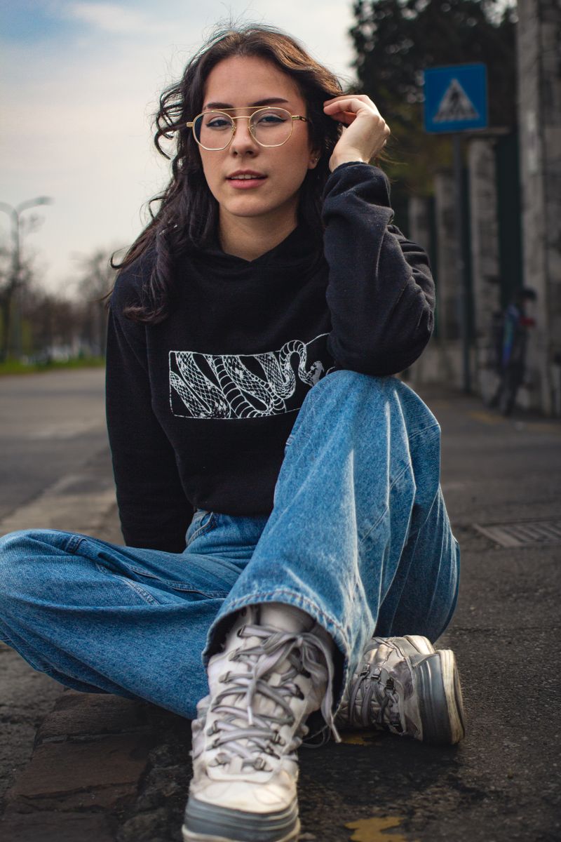 Young woman in a black hoodie and jeans sitting on a street