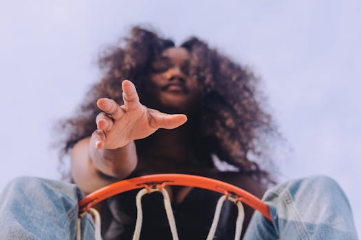 A dynamic low angle shot of a woman reaching towards a basketball hoop, emphasizing action and ambition.