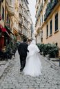Backs of Bride and Groom Walking Down a Narrow Street Between Buildings