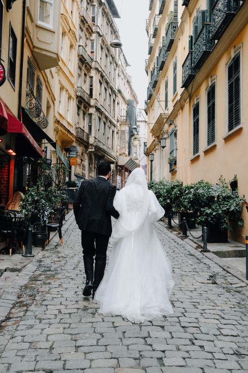 Free Bride and groom walking hand in hand on a charming cobblestone street lined with historic buildings. Stock Photo