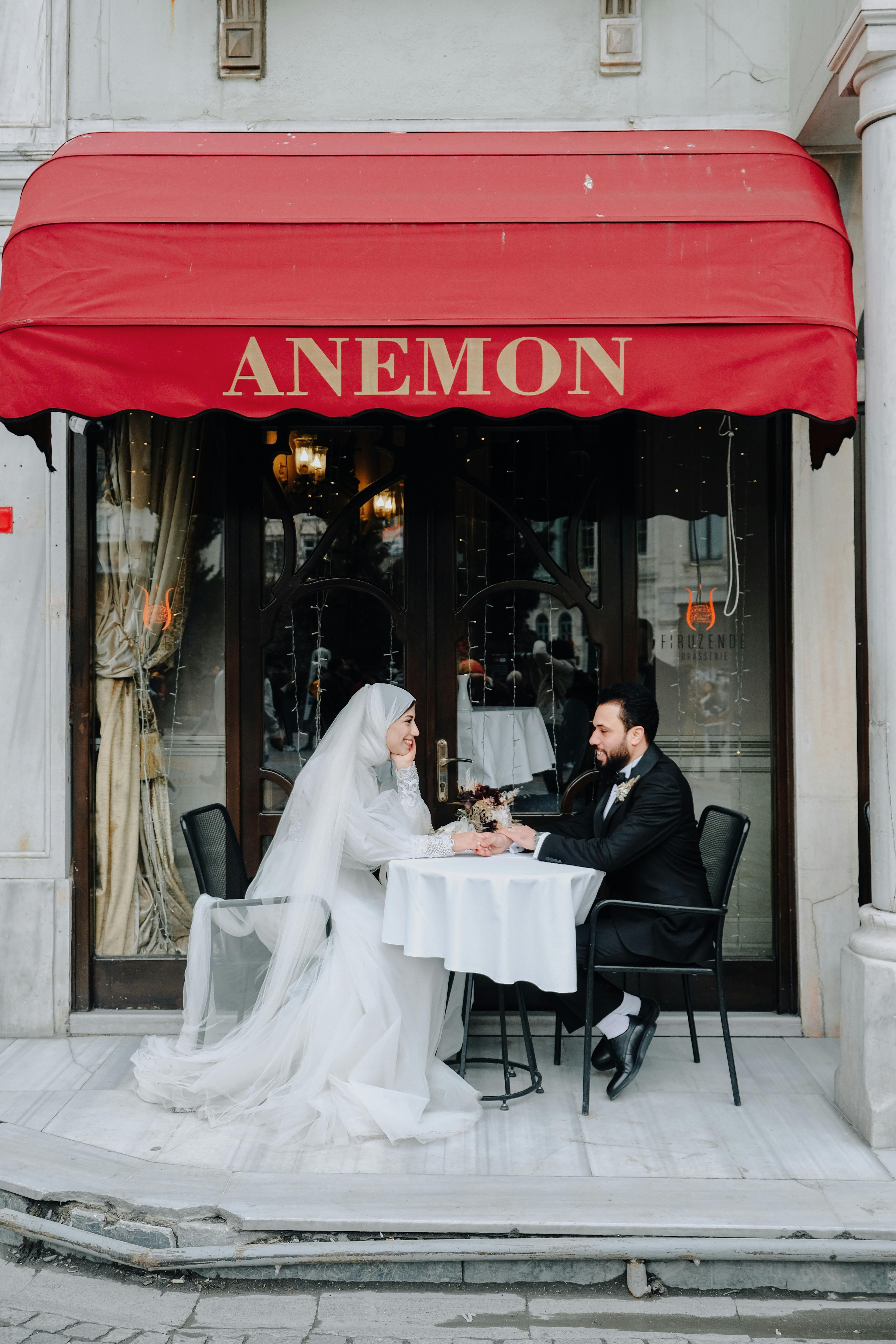 A bride and groom share a romantic moment at an outdoor café table, celebrating their wedding day.
