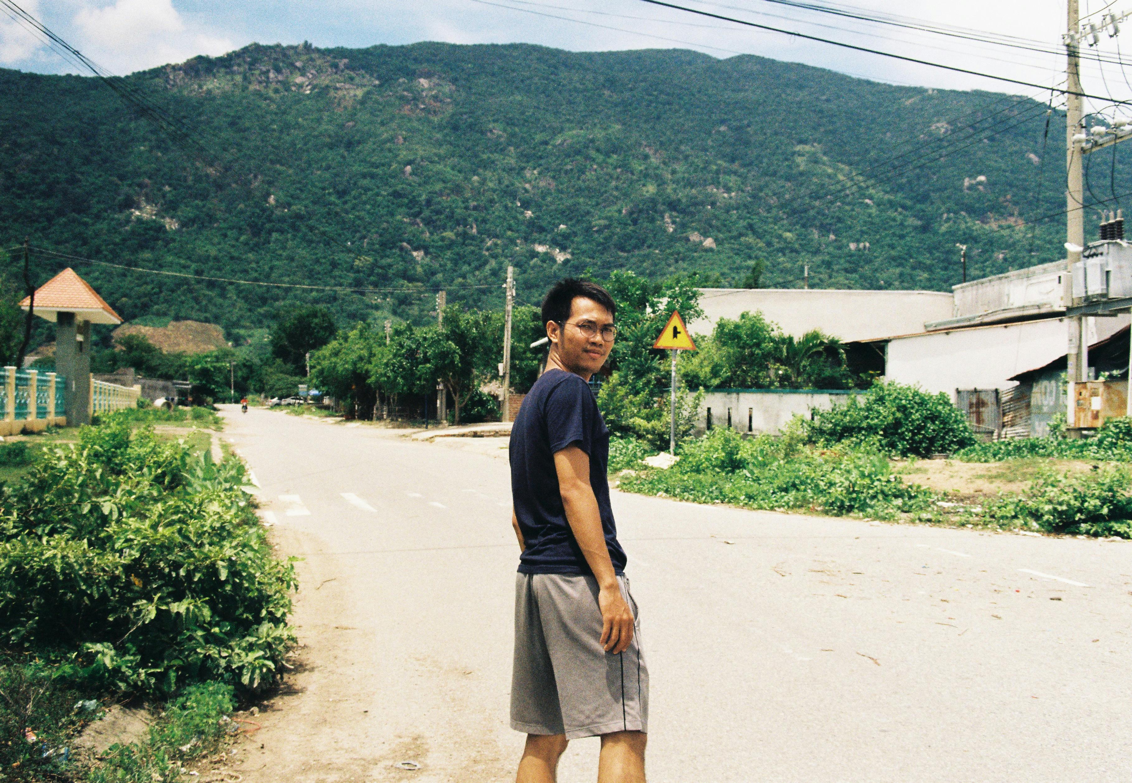 Asian man standing on a quiet rural road with hills in the background.