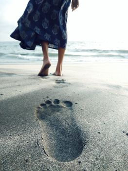 A woman walks on the beach, leaving footsteps in the sand by the ocean.