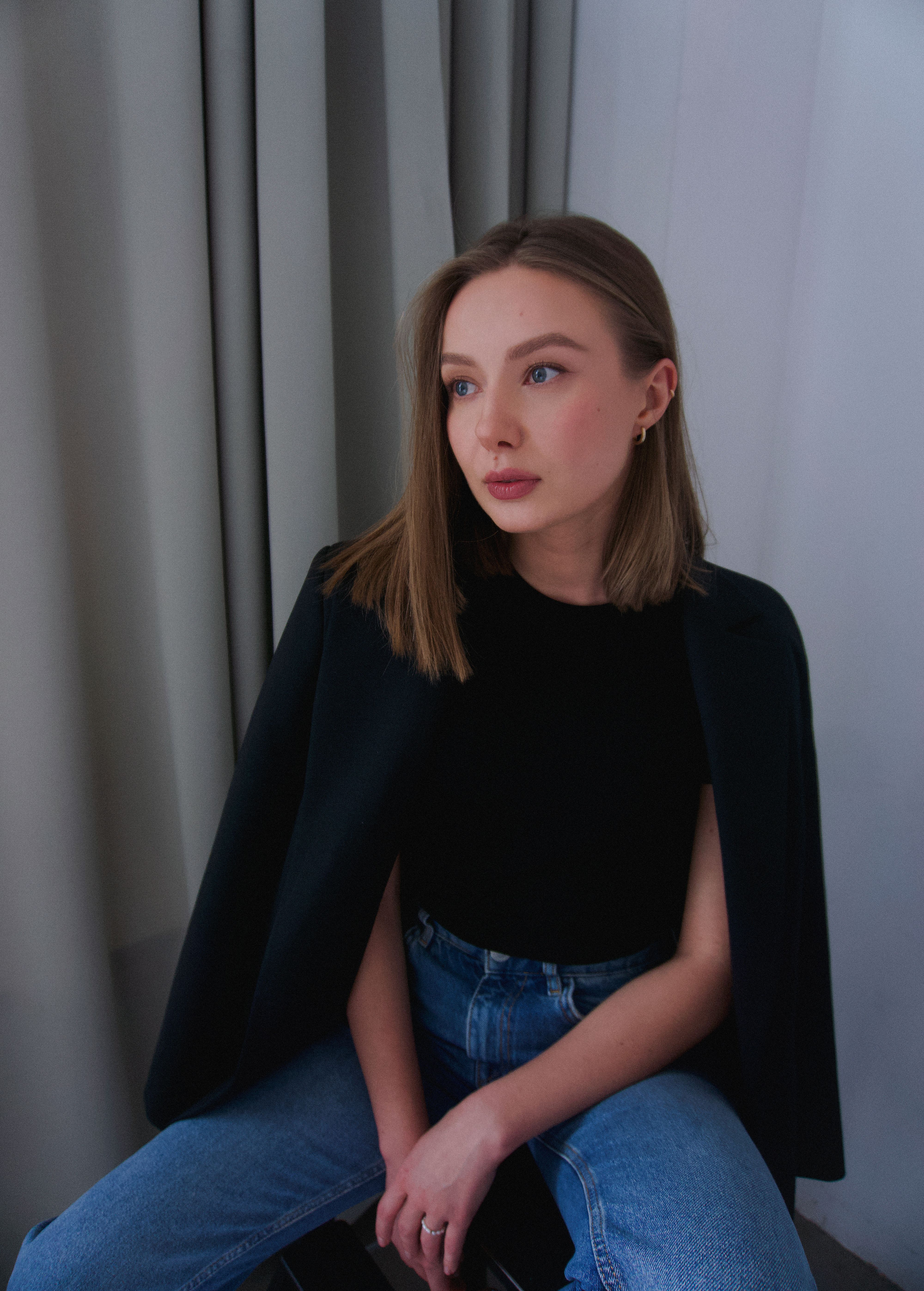 Stylish portrait of a young woman sitting indoors in a modern studio setting.
