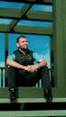 Man in Black and Gray Stripe Polo Shirt and Black Pants Sitting on Brown Wooden Bench