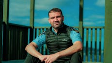 Man in Blue and Black Stripe Polo Shirt and Black Pants Sitting on Brown Wooden Bench