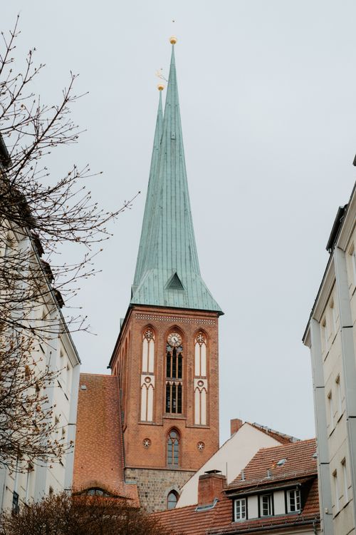 Free A picturesque Gothic church tower with copper roof, framed by city buildings. Stock Photo