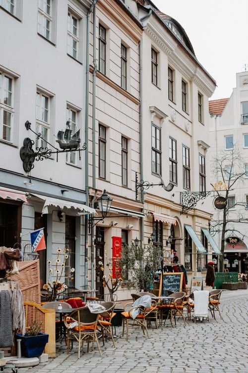 Free Quaint cobblestone street featuring empty al fresco café seating amidst classic European architecture. Stock Photo