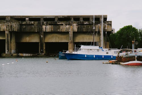 Free Blue and White Boat on Water Near Abandoned Concrete Building Stock Photo