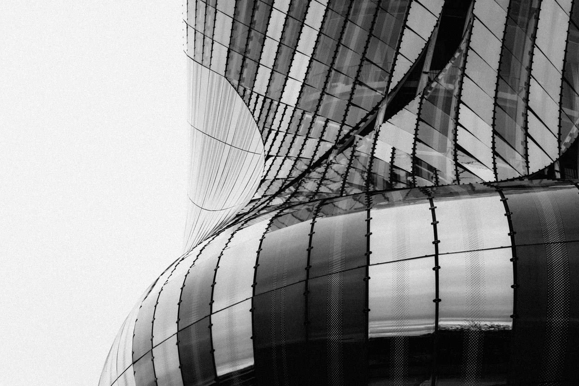 Black and white image of a futuristic building facade with curved glass and metal panels.