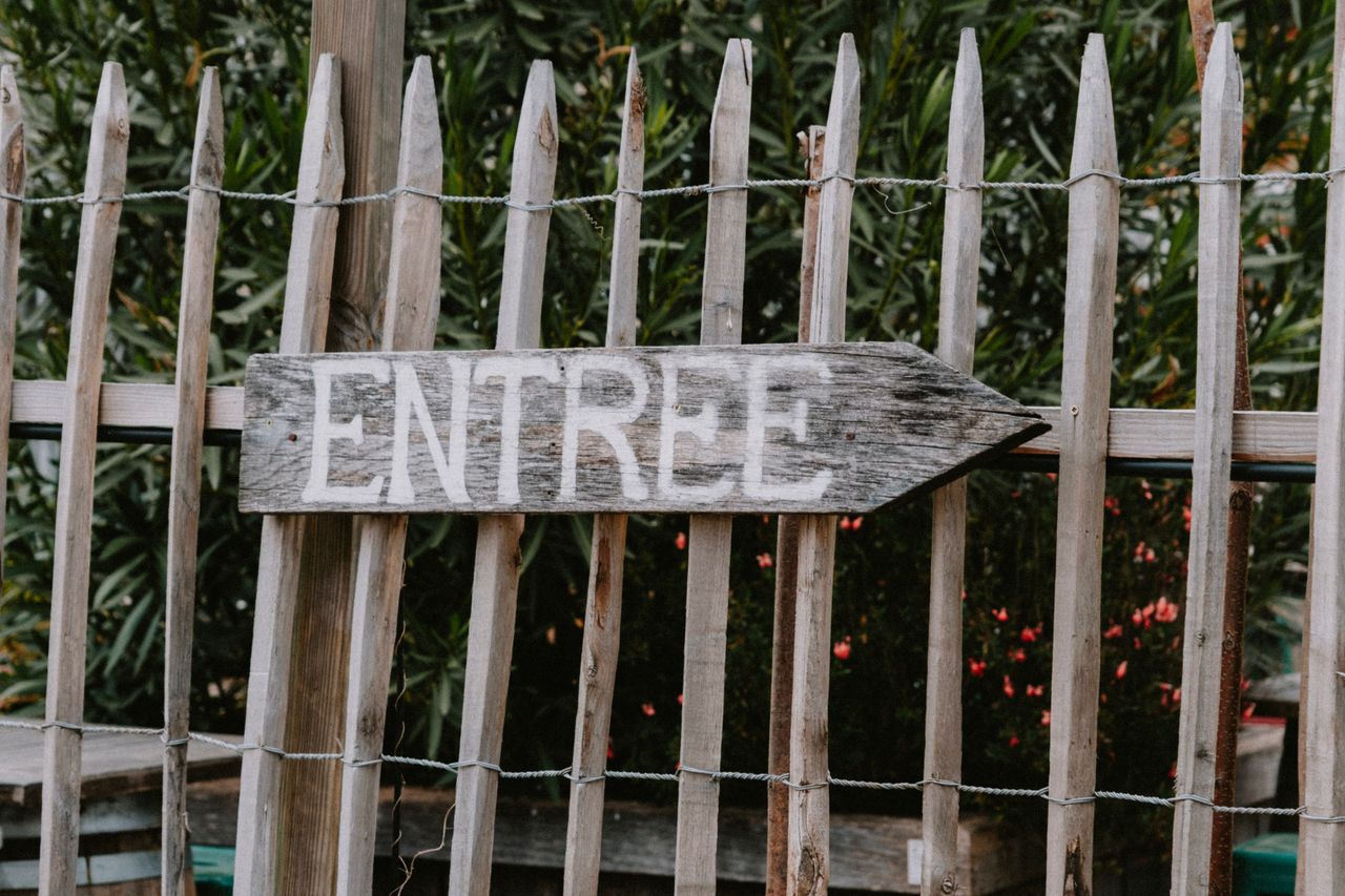 weathered wooden sign with the word entree pointing direction in a gar