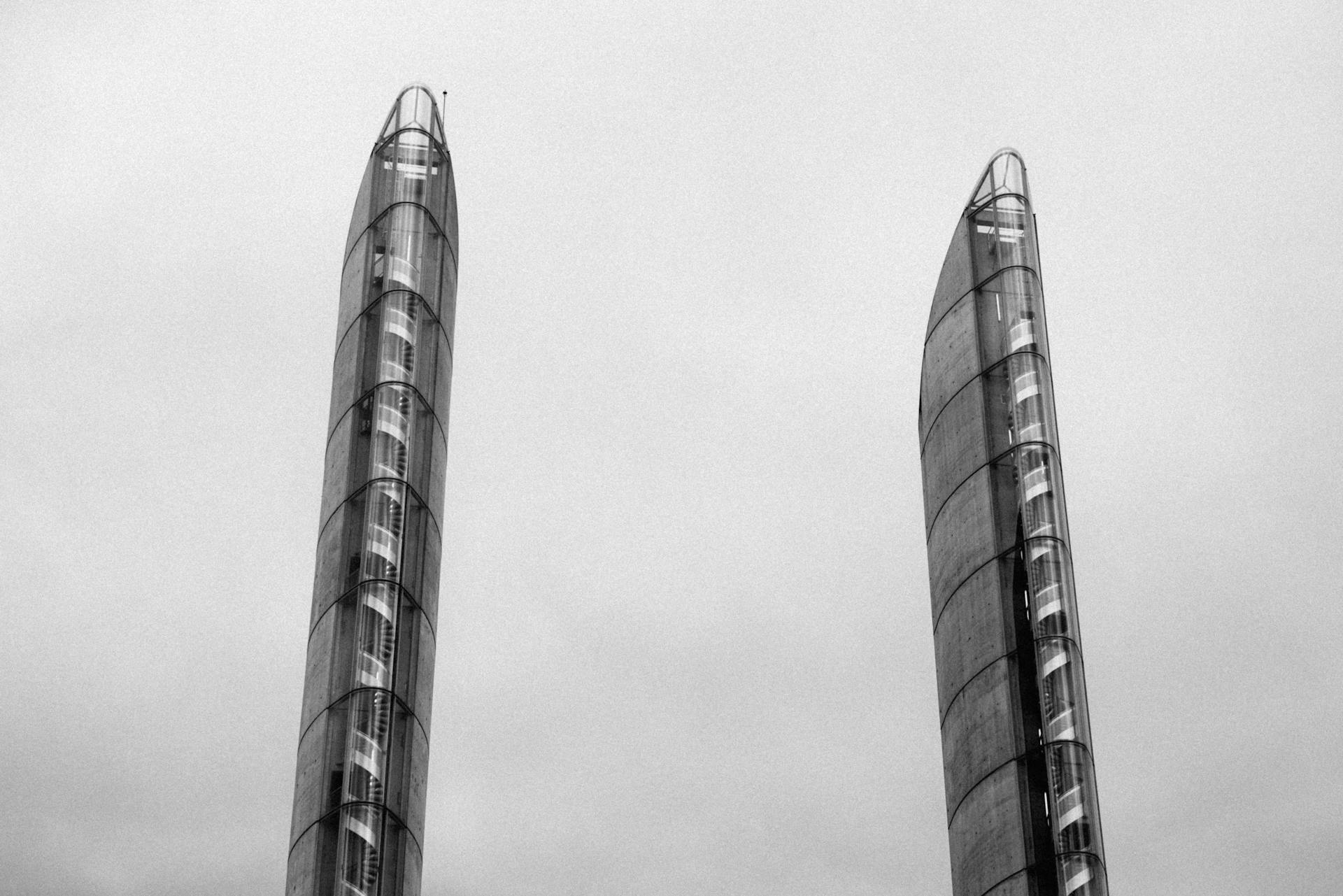 Monochrome view of modern spire-like skyscrapers reaching into a cloudy sky.