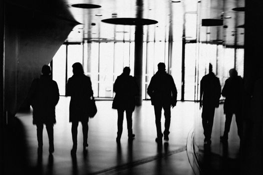 Group of silhouetted people walking indoors with reflective surfaces creating an abstract visual.