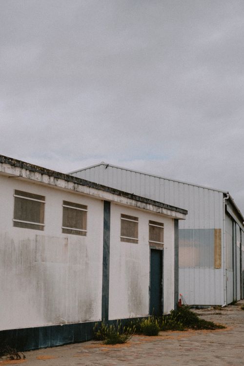 Free Exterior view of an abandoned industrial warehouse showcasing weathered walls and overcast sky. Stock Photo