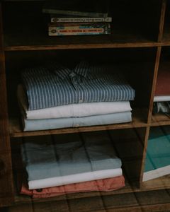 A tidy wooden shelf with neatly folded clothes and stacked books.