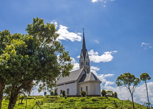Free A picturesque church with a steeple located on a hill surrounded by trees and blue sky. Stock Photo
