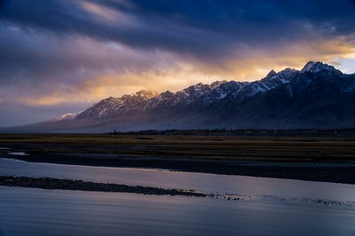 Free Stunning view of snow-capped mountains with a vibrant sunset sky reflecting on the river. Stock Photo