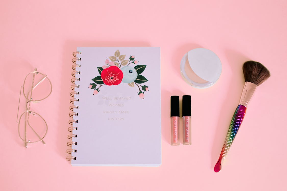 Flat lay Photography of Notebook Near Eyeglasses and Make-up