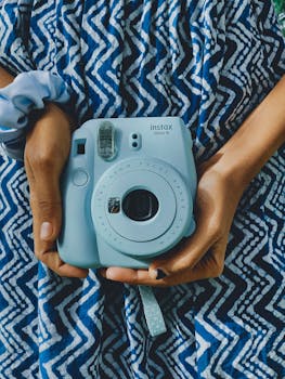 Hands holding a light blue instant camera against a patterned dress.