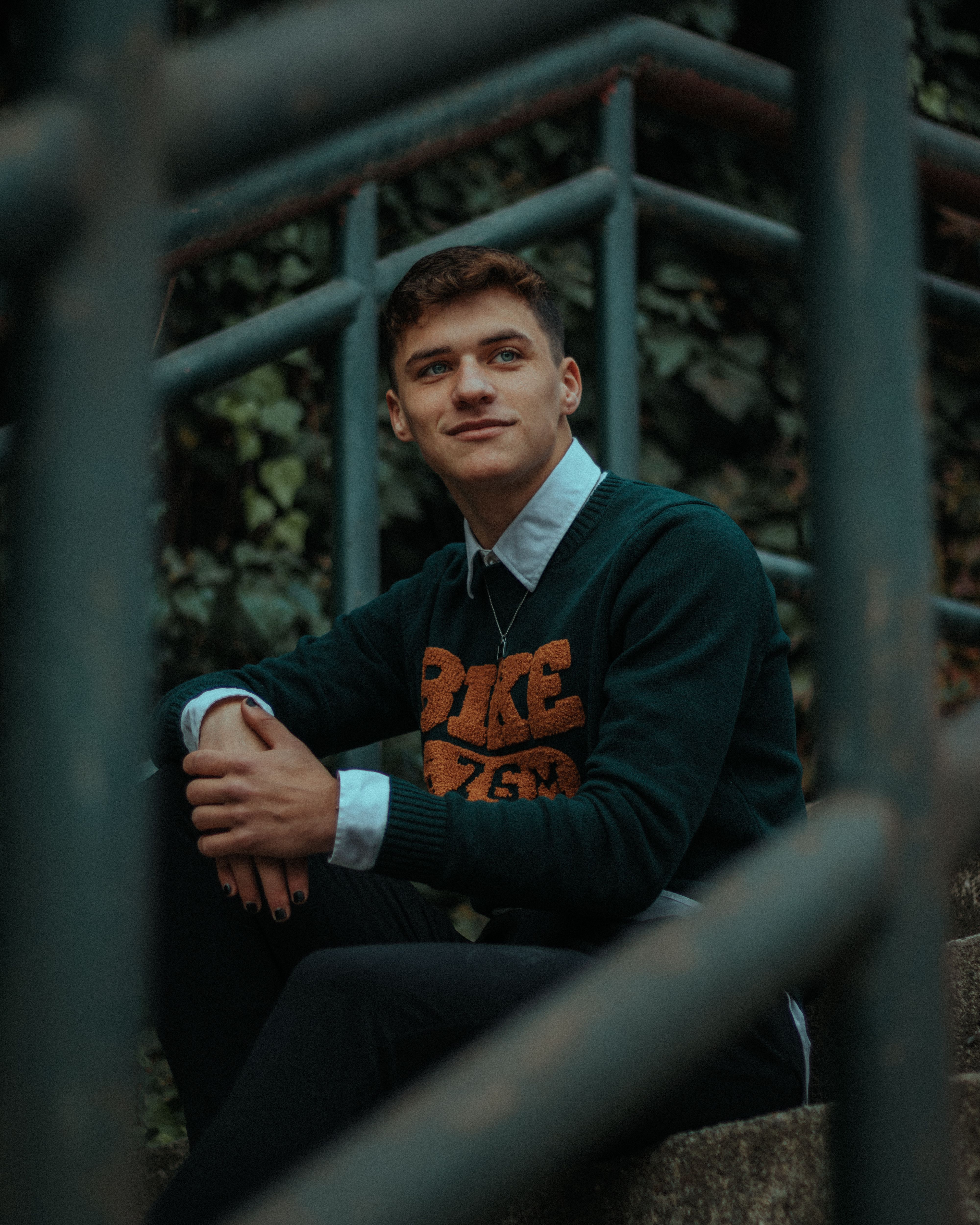Young man smiling while sitting on outdoor stairs surrounded by green foliage.