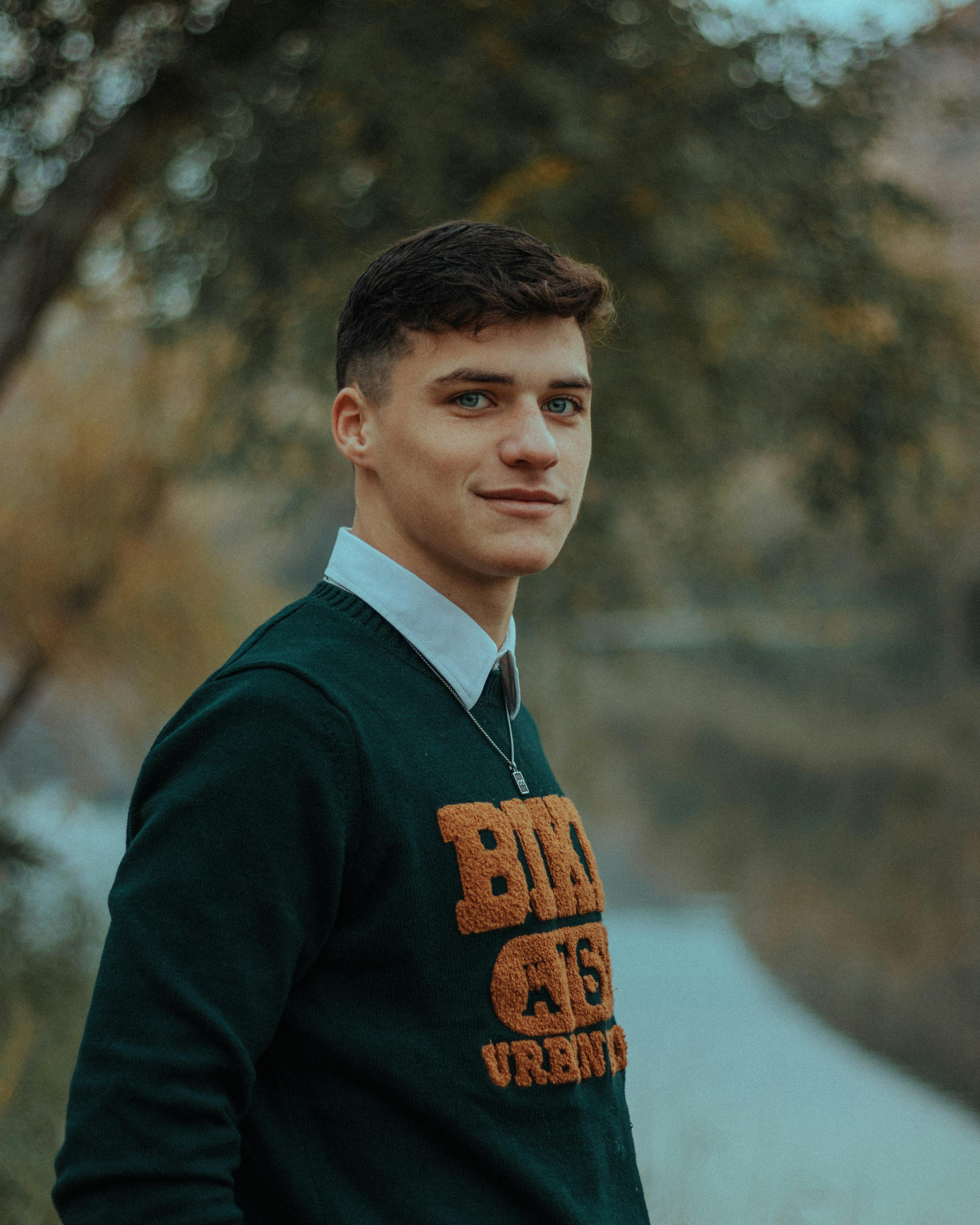 Portrait of a young man smiling outdoors with a blurred autumn background.