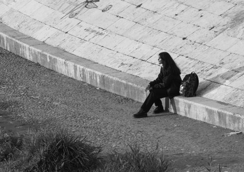 Free Black and white image of a woman sitting alone by a graffiti-covered wall in an urban setting. Stock Photo