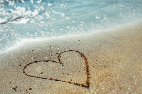 Free Heart shape drawn in sand with ocean waves gently approaching on a sunny beach day. Stock Photo