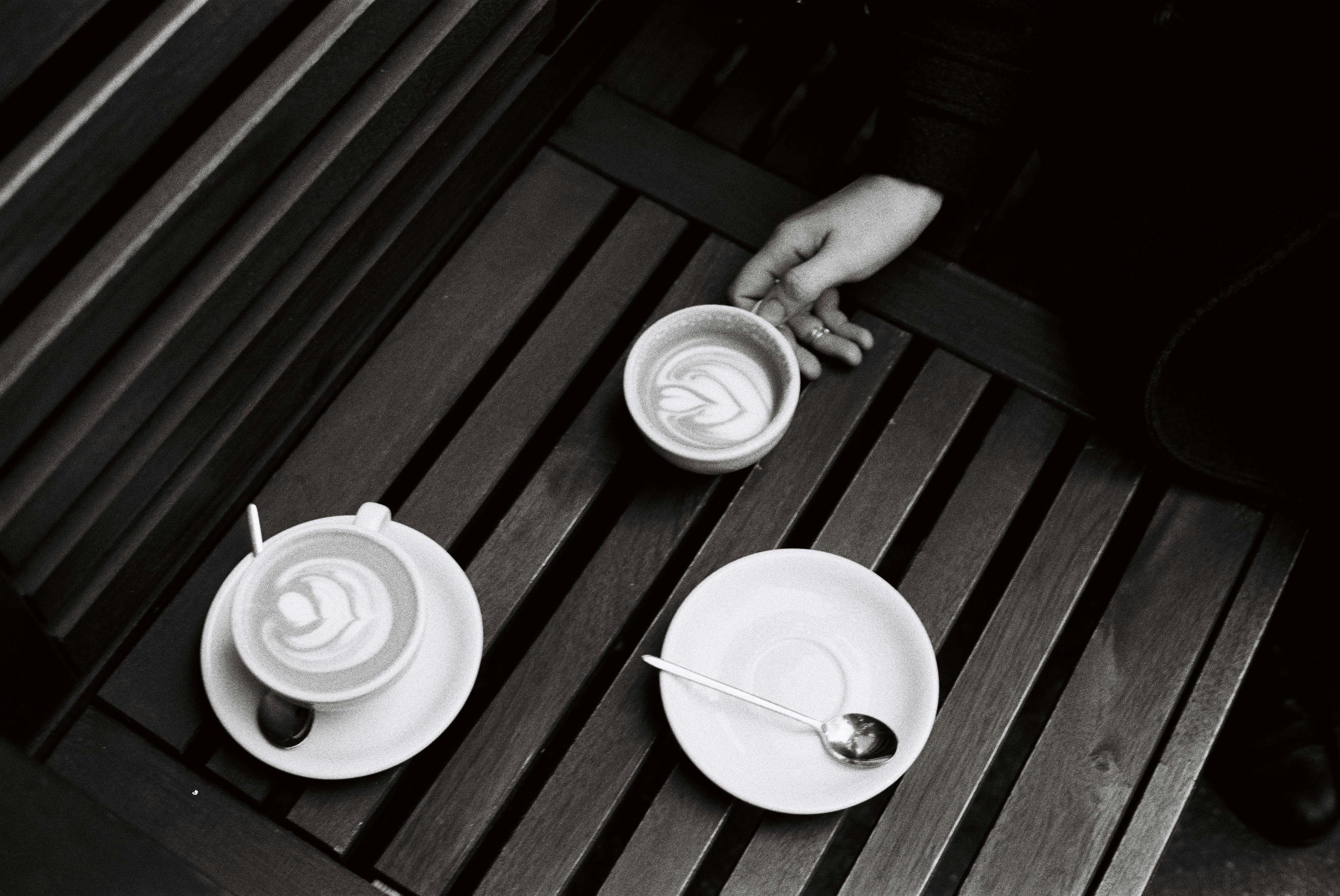 Elegant coffee art captured in black and white with cups and saucers on a wooden surface.