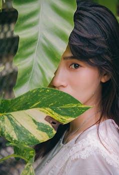 一位年轻女子脸部被大片绿叶遮住，散发着自然的美感
