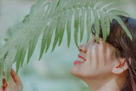 一位面带微笑的女性户外特写肖像，部分被新鲜的绿色蕨类植物叶子覆盖