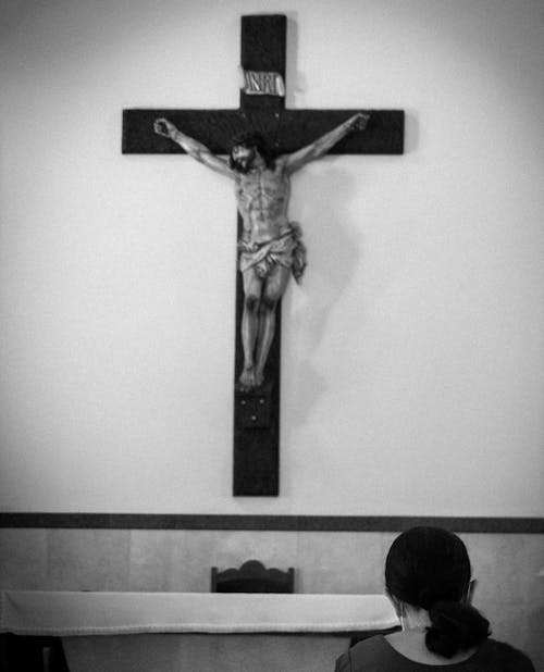 Grayscale Photo of a Woman Praying in front of a Crucifix