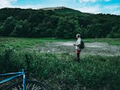 一名背着背包的男子站在风景优美的山地田野上，旁边停着一辆自行车，享受着大自然的美丽