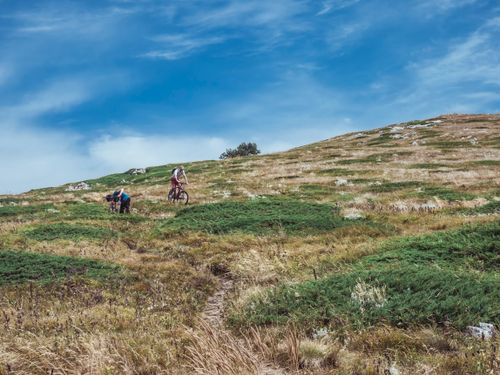 Free Two cyclists enjoying a ride on a scenic grassy hillside under a clear blue sky. Stock Photo