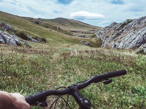 Person Riding Bicycle Overlooking Green Grass Field and Hill