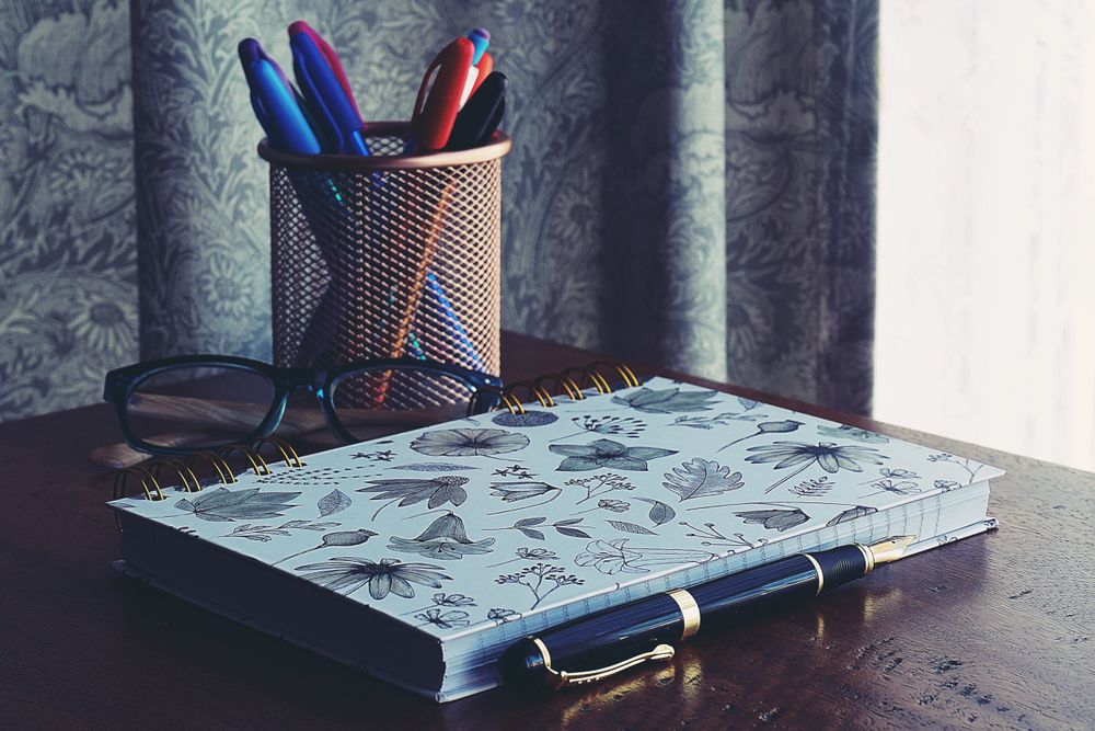 Notebook, pen, and glasses on a desk — photo by Suzy Hazelwood on Pexels