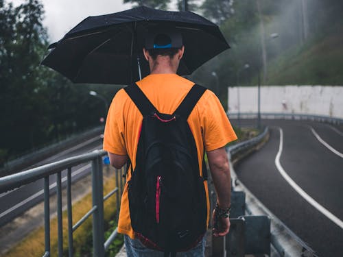 Man Wearing Orange Shirt Holding Black Umbrella