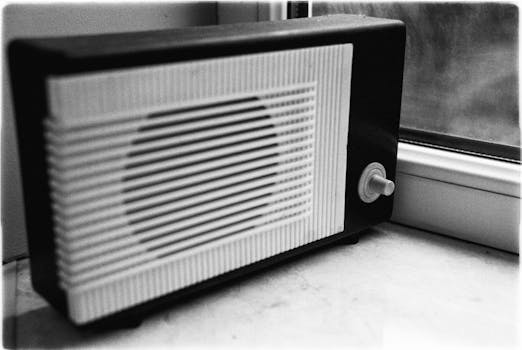 Black and white photo of a vintage radio placed on a windowsill, evoking nostalgia and retro vibes.