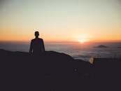 悬崖上，一个孤独的人影正望着云层之上生机勃勃的日落
