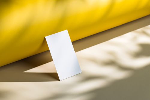 Free Blank white card in sunlight with shadows on yellow and beige backdrop, ideal for copy space. Stock Photo