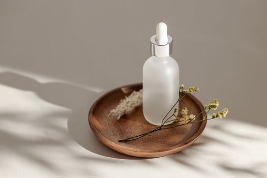 Elegant skincare bottle displayed on a wooden saucer with dried flowers and soft shadows.