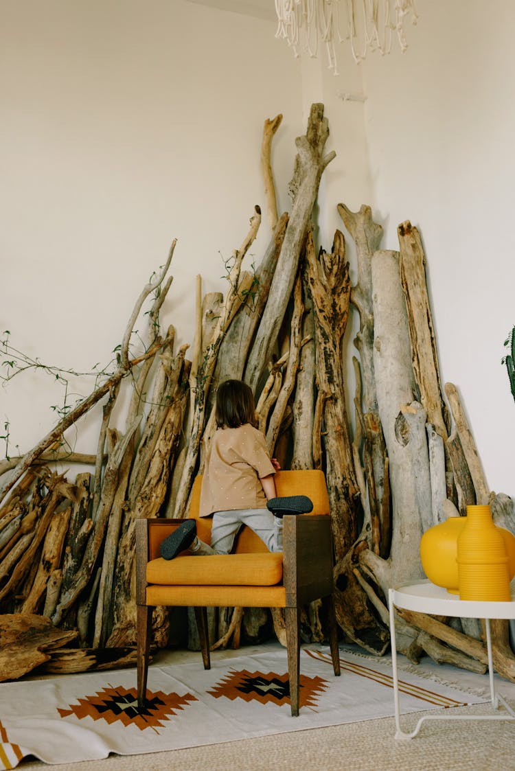 Child On An Armchair In An Interior With A Stack Of Wood 