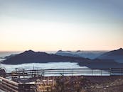 日出时分，薄雾笼罩的山谷与迷人的山脉景色尽收眼底，前景处可见木栏杆