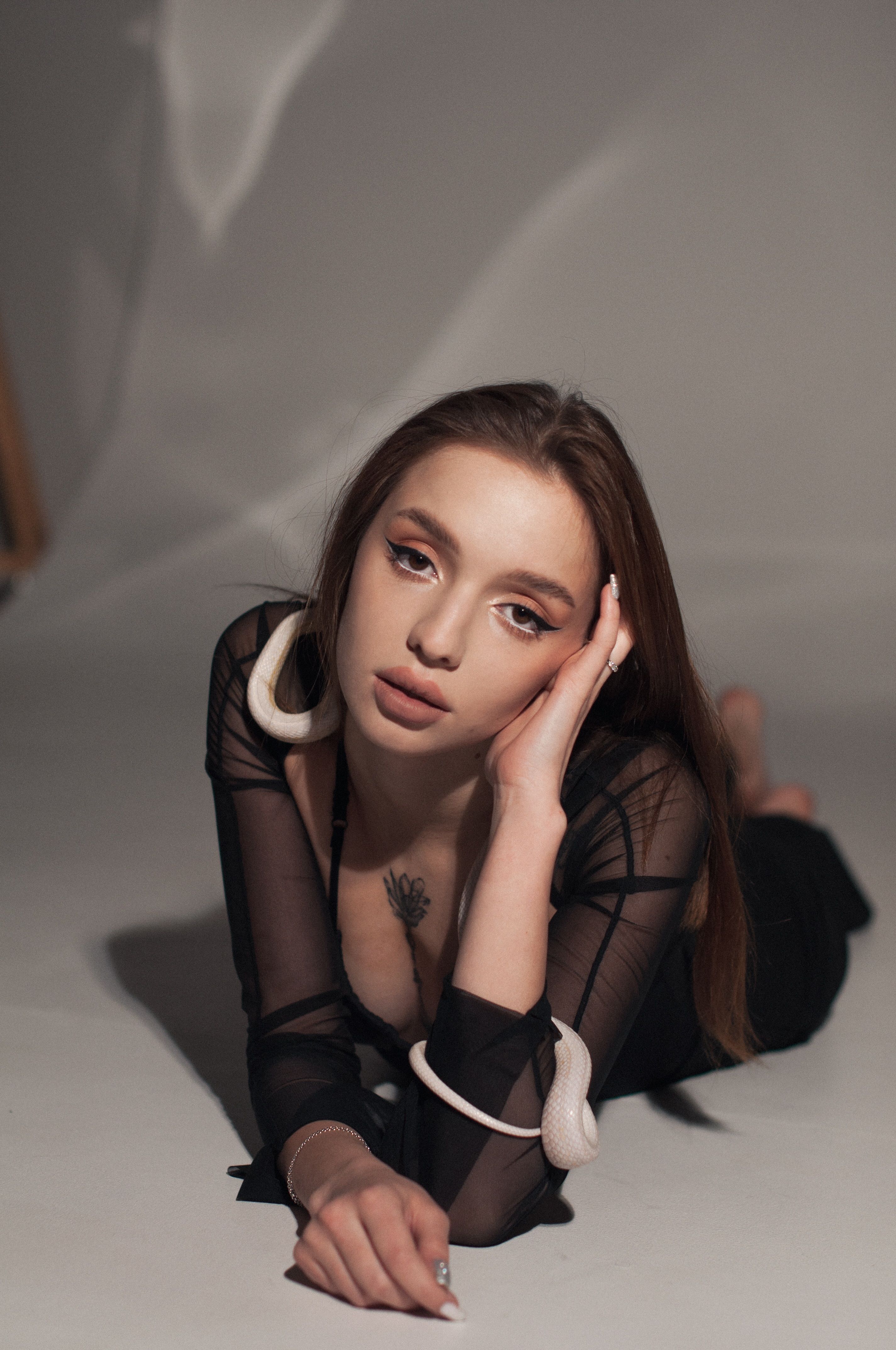 Fashionable woman with tattoos posing in a modern studio, showcasing a chic style and thoughtful expression.
