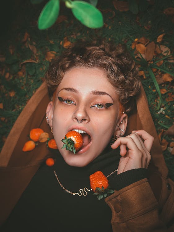 Free A Woman Lying on the Ground while Biting a Strawberry Stock Photo