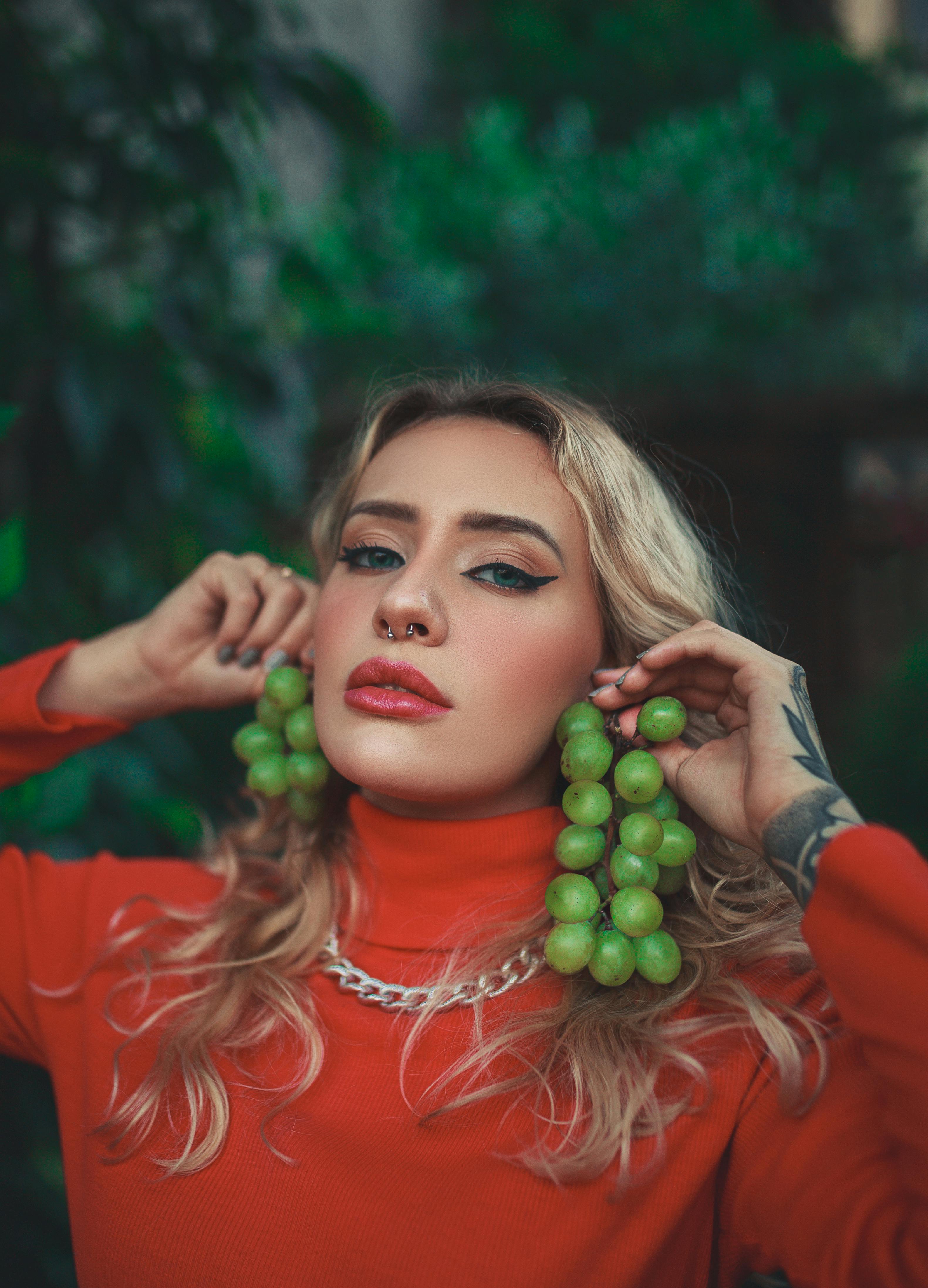 Stylish woman in red with unique grape accessories and tattoos in an outdoor setting.