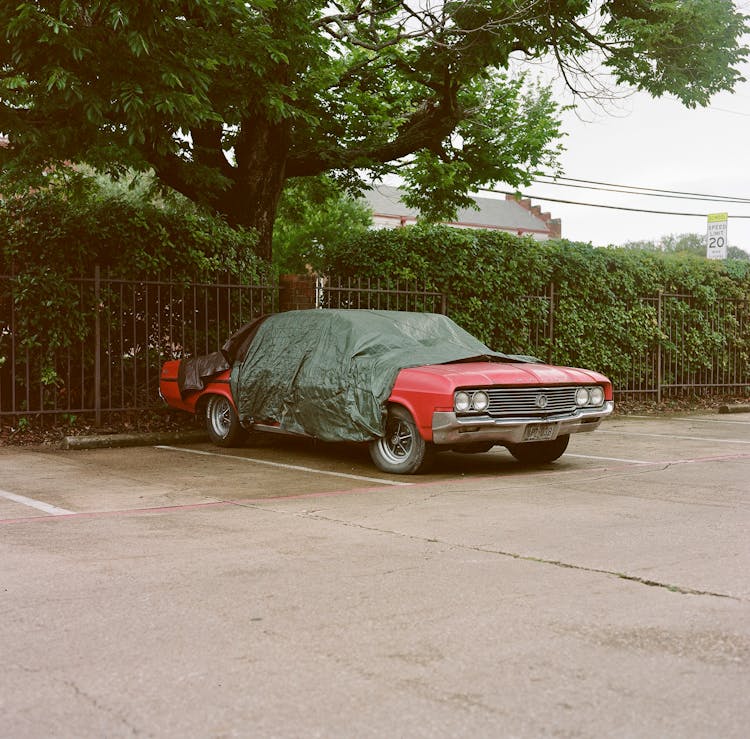 A Parked Red Car Covered With A Tarpaulin